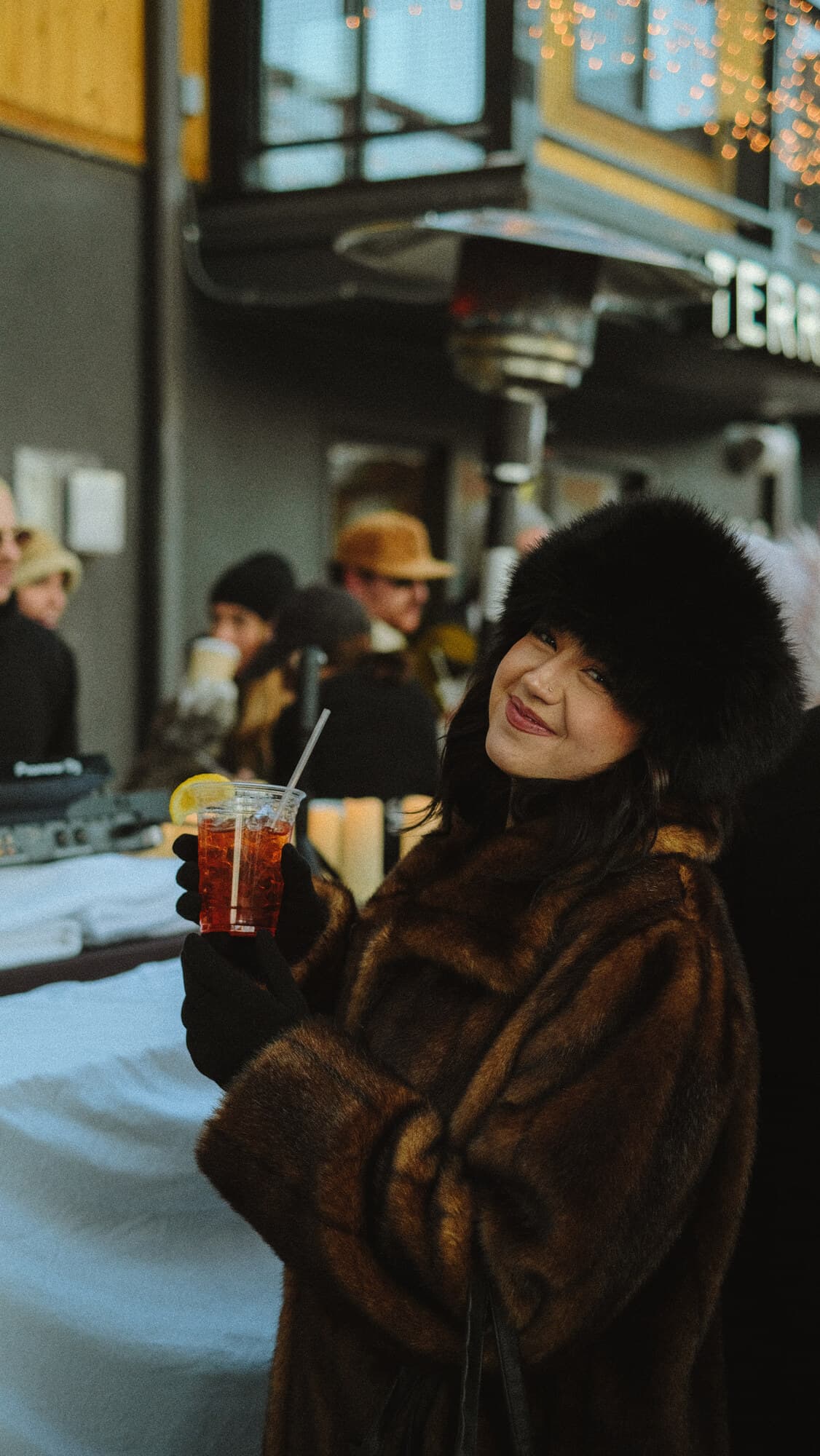 A guest in a fur coat raising a drink at an après ski night
